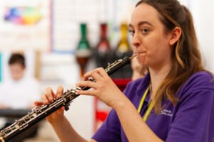 Young Associate Musician Tammy plays an Oboe. She is wearing a purple t shirt and the setting is a classroom. 