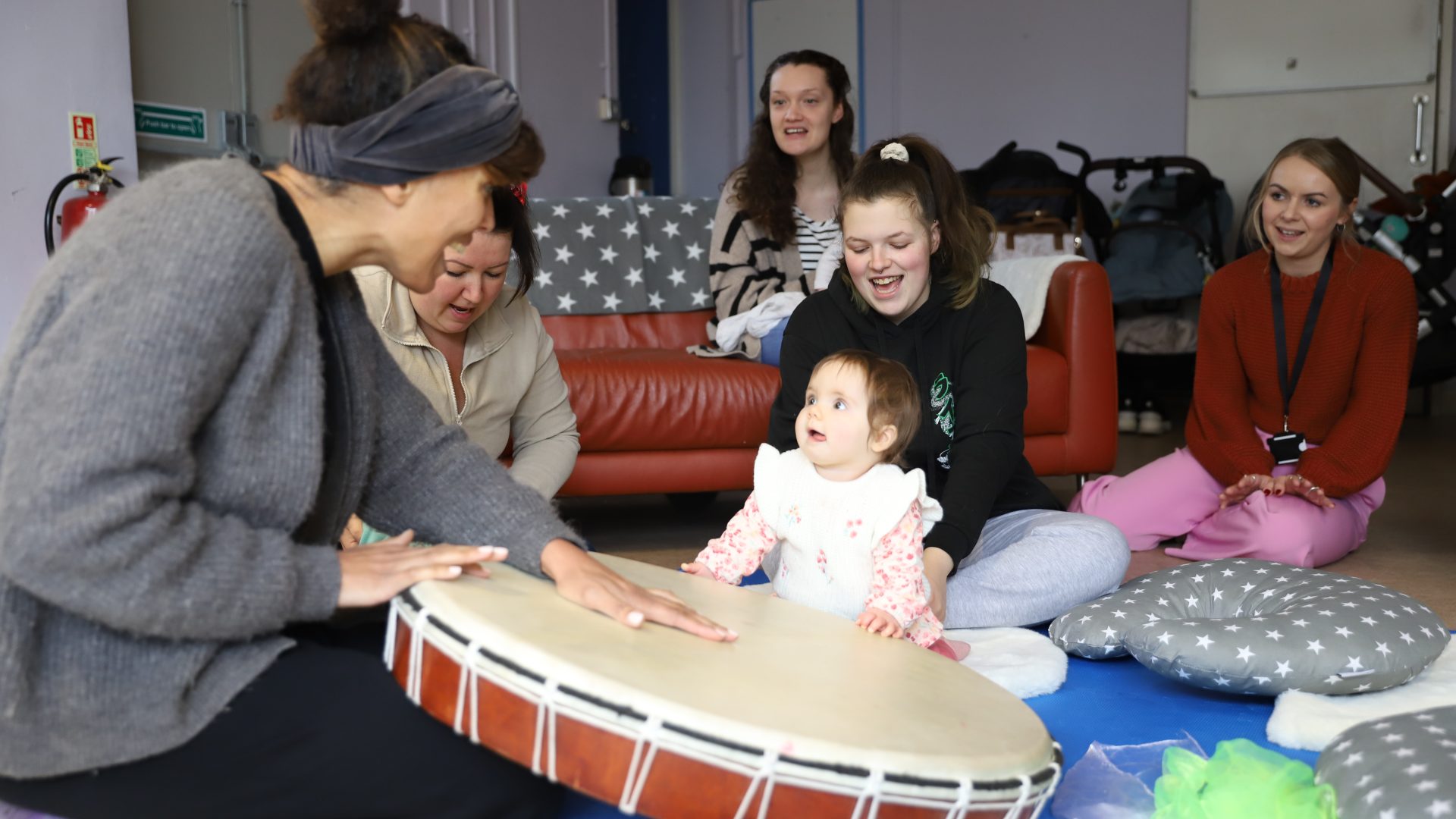 New bso associate musician, zoe palmer sitting with a big drum and a group of young mothers and babies looking at her.