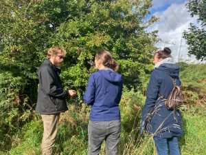 Upton Country Park Ranger, Rowan Booth, talks the team through tasks for the day. People standing against a hedge in the background. 