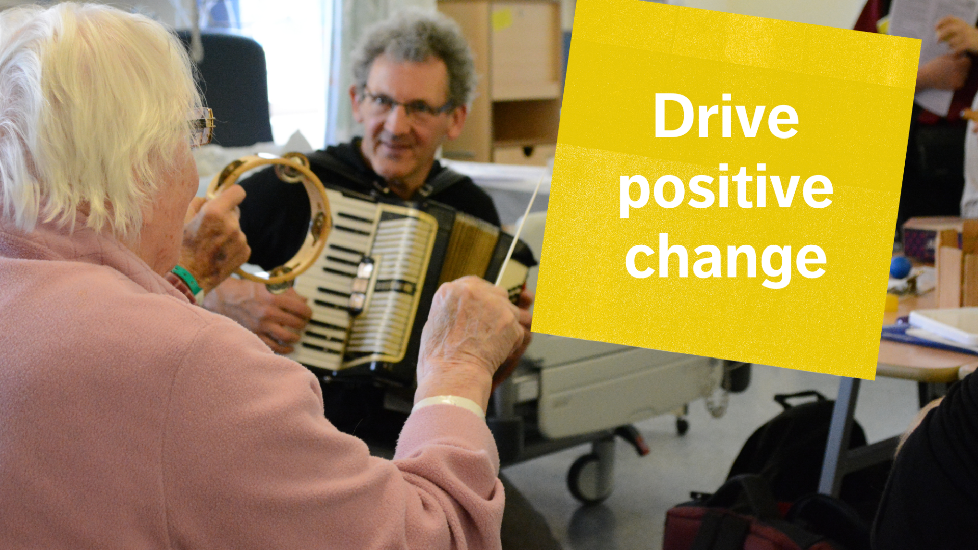 Elderly lady on hospital ward playing a musical instrument while community music leader plays guitar alongside her