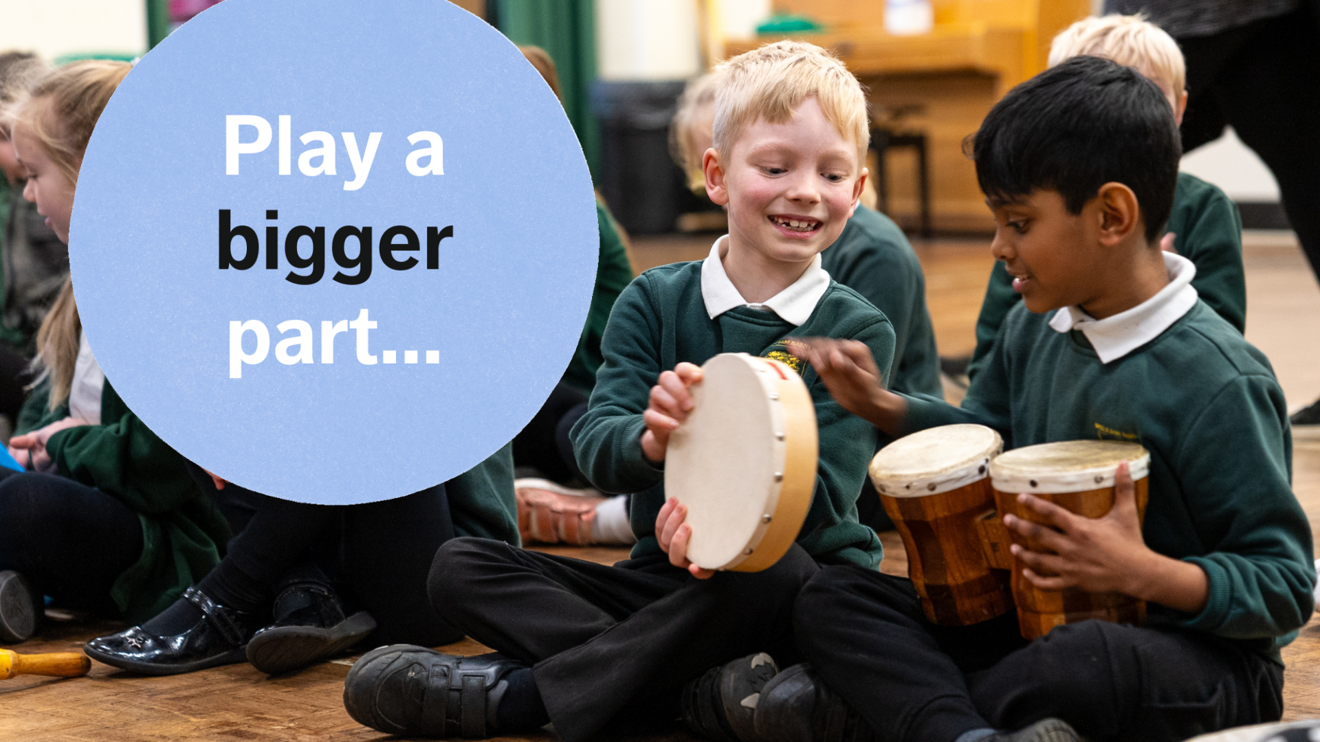 Two schoolchildren hold a tambourine and a set of bongos and play with the instruments together while smiling. A blue cartoon circle laid over the top of the image next to the children reads: "Play a bigger part"