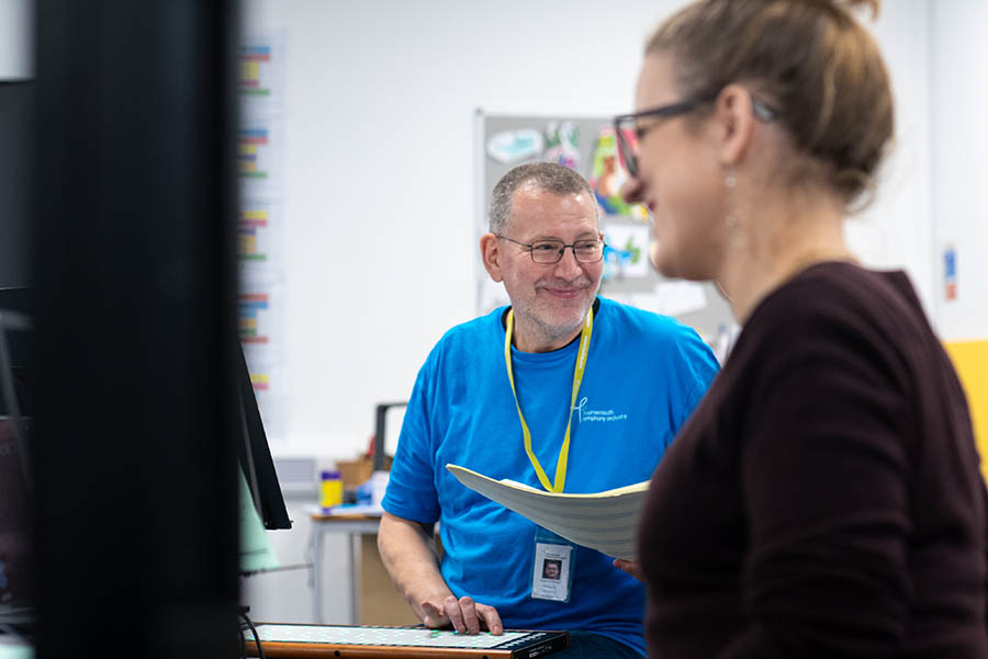 Musician wearing a blue t-shirt smiles at young players taking part in shared music-making. 
