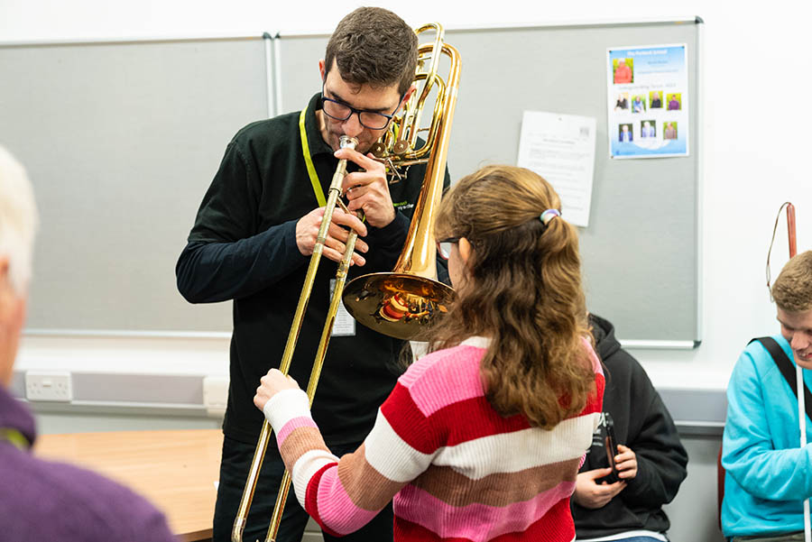 Musicians plays the trombone while young student touches the instrument to learn how it feels.