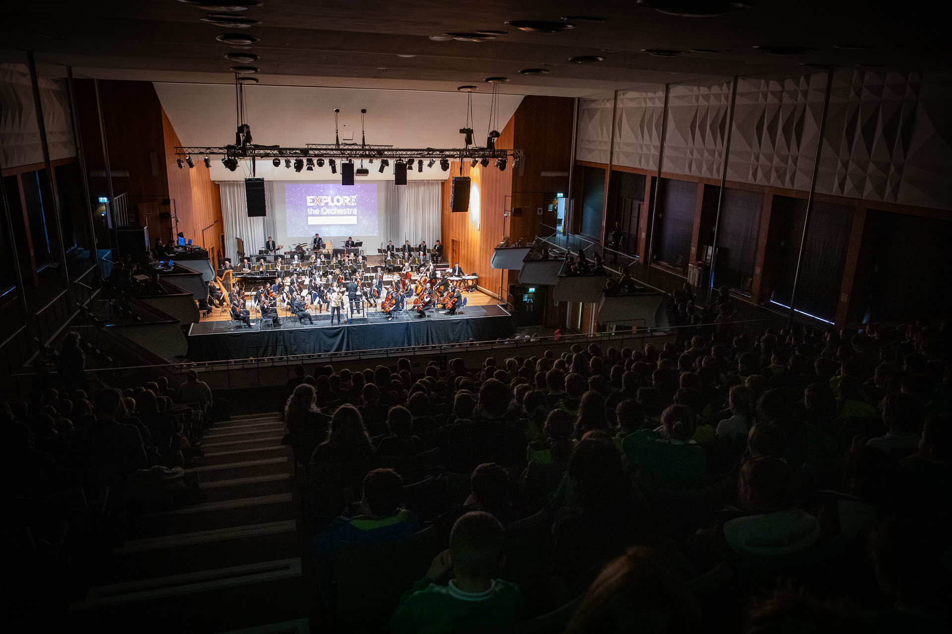 Orchestra and presenter perform a concert on stage to audience of hundreds of children