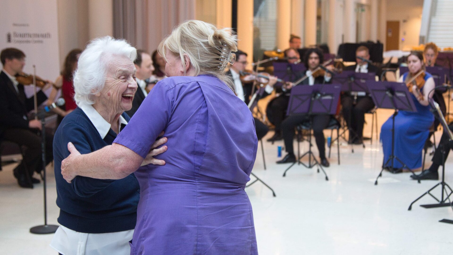 Two ladies are dancing in front of an orchestra