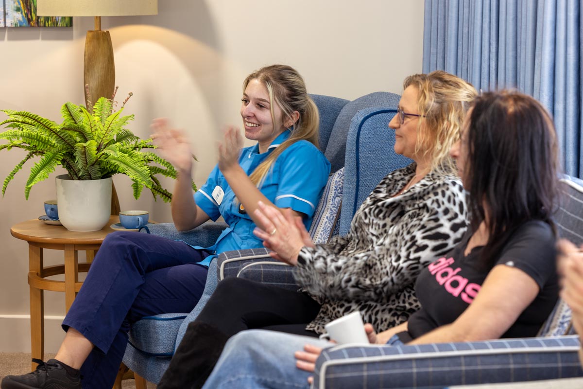 Three members of staff share a sofa and face a musician