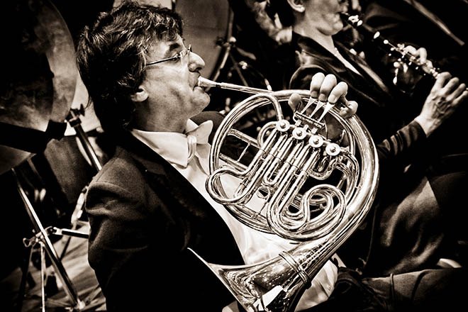 A man plays the french horn in concert dress.