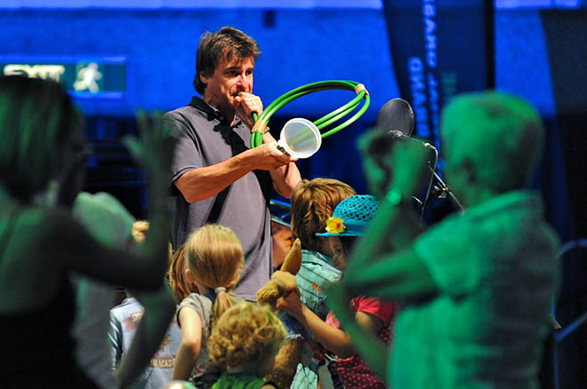 A man wearing smart casual clothing performs using a hosepipe instead of a french horn to an appreciative audience